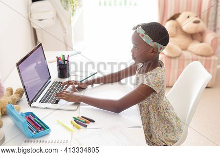 African american girl in bedroom at desk using laptop with copy space for online school lesson. staying at home in isolation during quarantine lockdown.