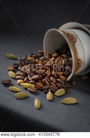 Aromatic Arabic coffee ingredients. Roasted coffee beans and whole green cardamom spilling out from a coffee cup.