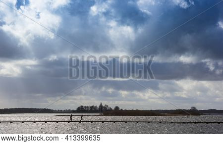 Dark Clouds Over The Lake In Roegwold, People Crossing The Wooden Jetty Between The Lakes In Groning