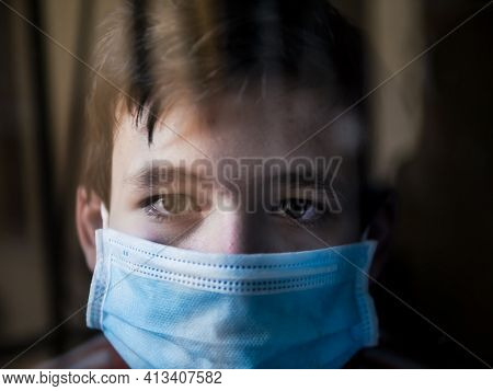 Boy With A Medical Mask Looks Sadly Out Of The Window During His Confinement Because Of Convid 19