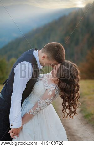 Beautiful Couple On Their Wedding Day Against The Background Of An Epithetical Sunset In The Mountai