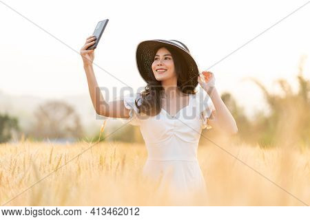 Happy Young Beautiful Woman Wearing Black Hat And White Dress Taking Selfie While Walking In The Gol