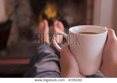 Nohy oteplování na krb s ruce držící kávy