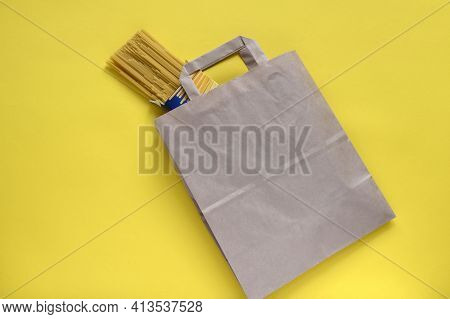 Pasta In Recycled Brown Paper Shopping Bag With Handle. Package On Yellow Background, Flat Lay, Mock