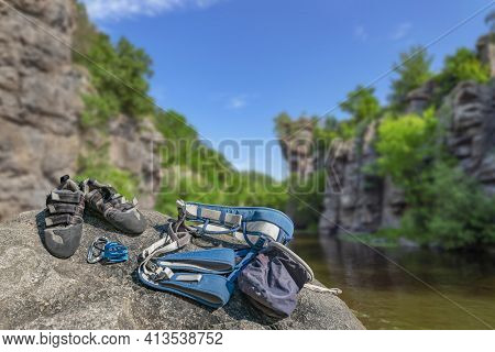 Climbing Gear Equipment On Rock On Blurred River Canyon Background. Climb Shoes, Belaying Carabiners