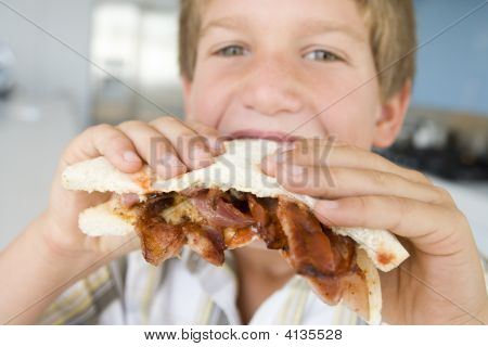 Giovane ragazzo In cucina mangiare Bacon Sandwich