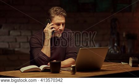 Older man tele working with laptop computer at home office in dark room, thinking, looking busy.
