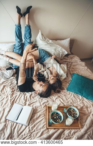 Caucasian Couple Are Sitting In Bed Upside Down Making A Selfie Before Eating Cereals With Milk