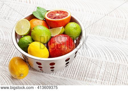Various fresh citrus fruits in colander. Bood orange, lime, lemon. On wooden table with copy space