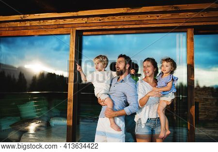 Family With Small Children Standing By Wooden Cabin, Holiday In Nature Concept.