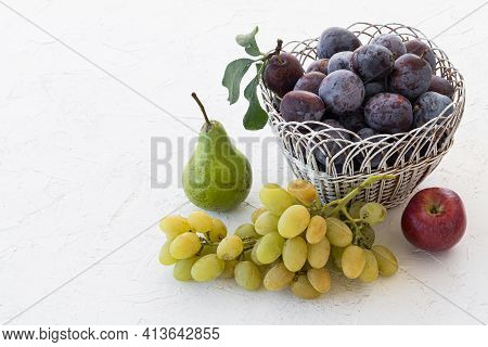 Just Picked Ripe Plums In A Wicker Basket And A Bunch Of Ripe White Grapes, An Apple, A Pear On The 