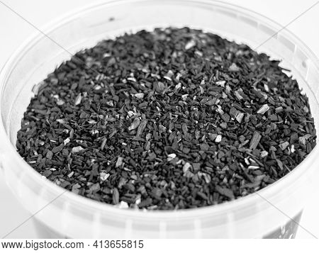 Small Black Charcoal In A Transparent Round Container On A White Backdrop. Close-up. Macro. A Sample