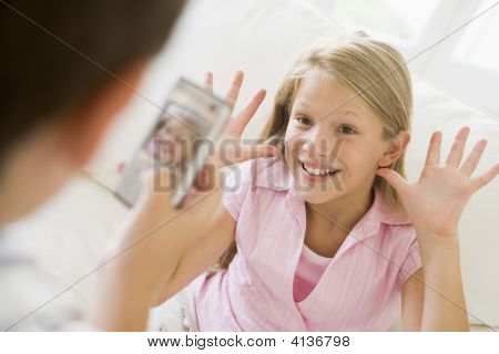 Giovane ragazzo prendendo foto di sorridente ragazza giovane con la fotocamera del telefono in casa