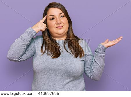 Beautiful brunette plus size woman wearing casual clothes confused and annoyed with open palm showing copy space and pointing finger to forehead. think about it. 