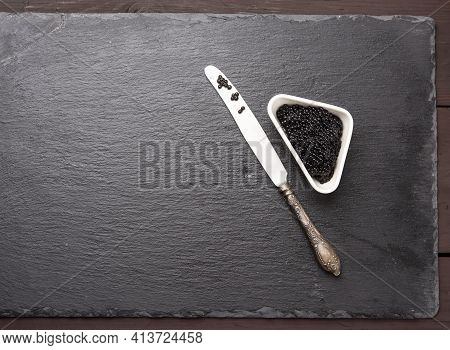 Black Grainy Caviar Of Paddlefish Fish In A White Ceramic Bowl, Black Background, Top View, Copy Spa