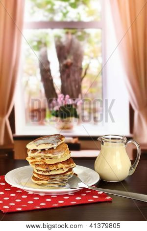 หวาน pancakes บนแผ่นกับนมข้นบนโต๊ะในห้อง