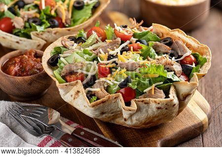 Taco Salad With Tomato, Lettuce, Black Olives, Cheese And Pork In A Tortilla Shell On A Wooden Board