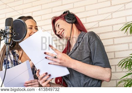 Low Angle Of Happy Voice Actresses With Scripts Laughing At Joke And Looking At Each Other While Pre