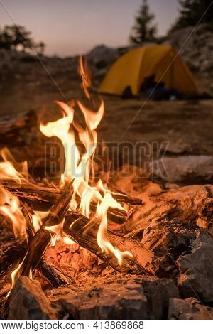 Bonfire burning in tourist camp in mountains. Beautiful campfire, burning wood by tent in summer evening. Active lifestyle, traveling, hiking and camping concept. Campfire burning in slow motion