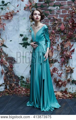 Full length portrait of a beautiful sophisticated girl in an elegant dress standing by the old vintage wall. Hair and makeup in the style of the 20s. 