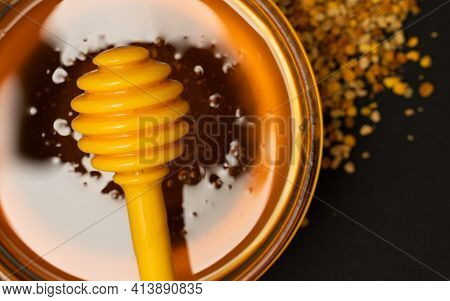 A Yellow Spoon Of Honey Dipped In A Jar Of Honey And Bee Bread Scattered On A Black Background. Hone