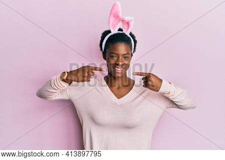 Young african american girl wearing cute easter bunny ears smiling cheerful showing and pointing with fingers teeth and mouth. dental health concept. 