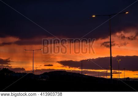 Spectacular Red Sunset With Dark Rainy Clouds Over The Bridge With Silhouettes Of People And Vehicle