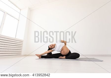 Young Flexible Pregnant Woman Doing Gymnastics On Rug On The Floor On White Background. The Concept 