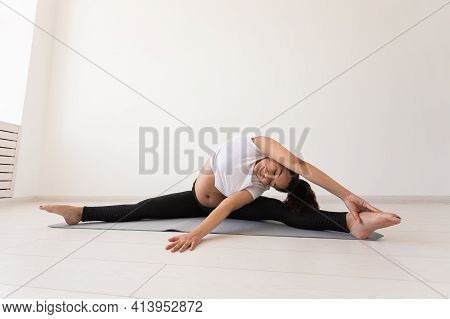 Young Flexible Pregnant Woman Doing Gymnastics On Rug On The Floor On White Background. The Concept 