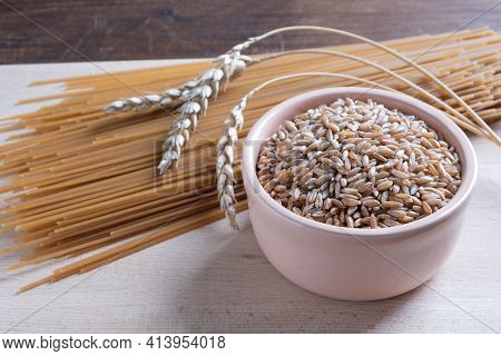 Spelt Spaghetti And Bowl With Uncooked Spelta Grain And Ears On Wooden Table.
