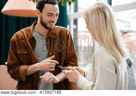 Happy young couple talking while standing insode cafe, holding mobile phone