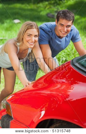 Smiling couple pushing their broken down car together