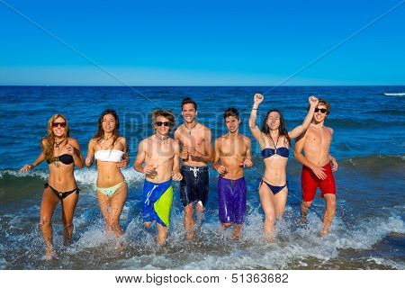 Teenagers group running happy splashing on the beach in summer vacations