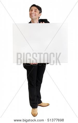 Businessman or salesman in a smart suit standing with a toothy ingratiating grin holding a blank sign in his hands with copyspace for your text or advertisement