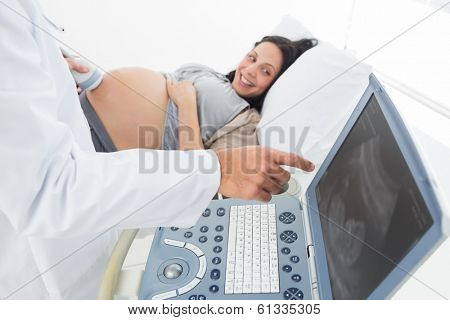 Midsection of male doctor showing ultrasound monitor to pregnant woman in hospital