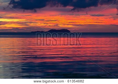 Dramatic fiery orange and red sunset in Siquijor in the Philippines with a mangrove tree silhouetted against the glowing horizon under heavy stormy cloud cover