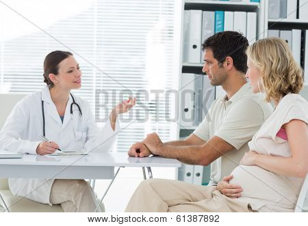Female gynaecologist discussing with expectant couple in clinic