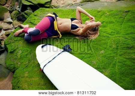 Sexy surfer girl lying on beautiful moss rock resting after surfing
