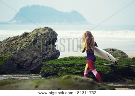 Beautiful surfer girl walking in the beach carrying her surfboard