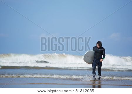 Professional surfer dressed in wetsuit going out of the water after surfing
