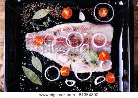 Pangasius fillet with spices and vegetables on firepan and wooden table background