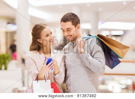 sale, consumerism, technology and people concept - happy young couple with shopping bags and smartphone talking in mall