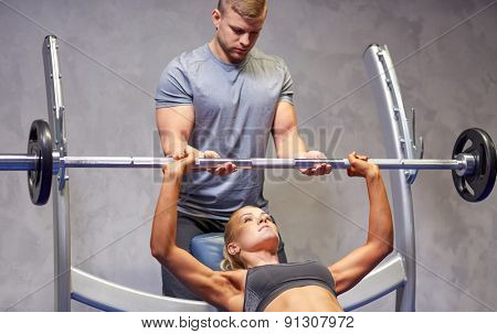 sport, fitness, teamwork, bodybuilding and people concept - young woman and personal trainer with barbell flexing muscles in gym