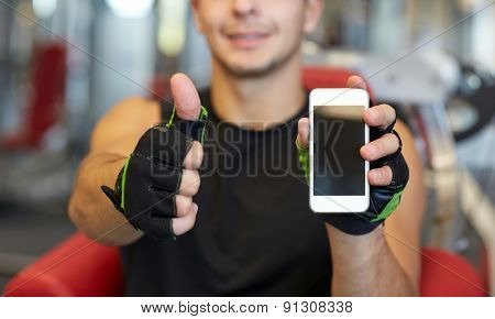 sport, bodybuilding, lifestyle, technology and people concept - happy young man with smartphone showing thumbs up in gym