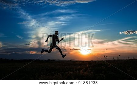 Silhouette Man Running And Jumping, On Meadow, Sunrise -sundown Sky At Background. Runner - Sprinter