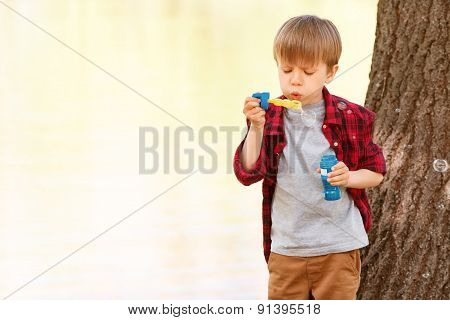 Little boy blowing bubbles in front of tree