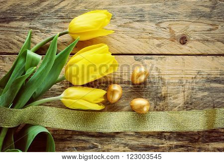 Easter background with yellow tulips three golden eggs on old wooden table