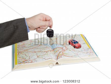 Male hand with car key over an open old road atlas and small red toy car on atlas on a light background