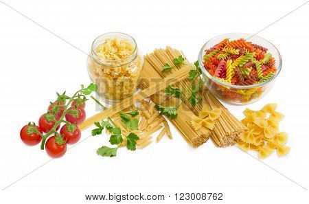 Uncooked dried long pasta two varieties colored spiral pasta farfalle mostaccioli creste di galli sprigs of parsley and cluster of cherry tomatoes on a light background