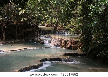 Cascades with clear turquoise water and jungle around in National park Kuang Si Waterfall Lao.